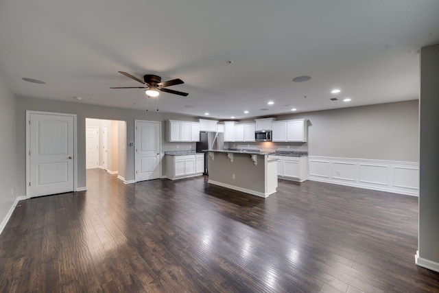 kitchen featuring appliances with stainless steel finishes, a center island, a kitchen bar, dark wood-type flooring, and recessed lighting