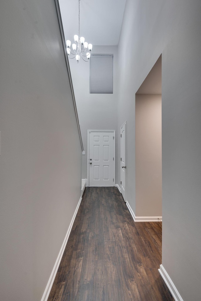 hallway featuring a chandelier, dark wood-type flooring, and baseboards