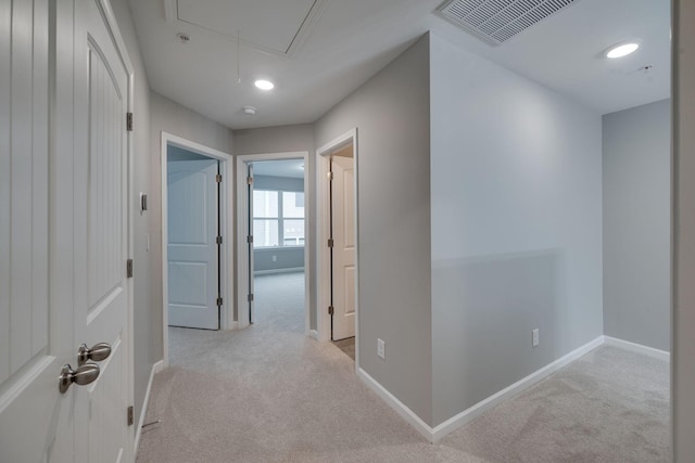 corridor featuring attic access, light colored carpet, and baseboards