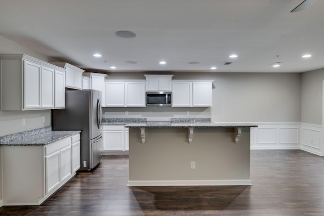 kitchen with stainless steel appliances, a kitchen bar, white cabinets, light stone counters, and dark wood-style flooring