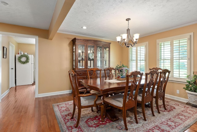 dining room with a textured ceiling, a chandelier, light wood-style floors, baseboards, and crown molding