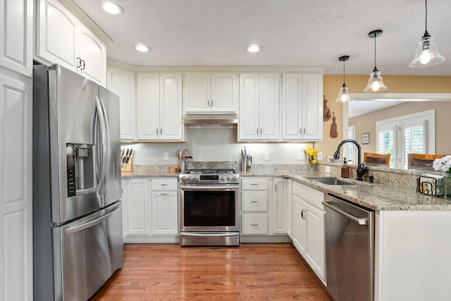 kitchen with stainless steel appliances, a sink, under cabinet range hood, a peninsula, and decorative light fixtures