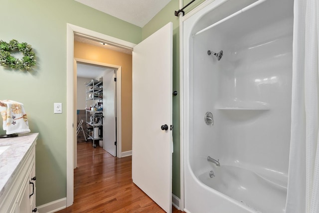 bathroom with wood finished floors, shower / bath combination, vanity, and baseboards