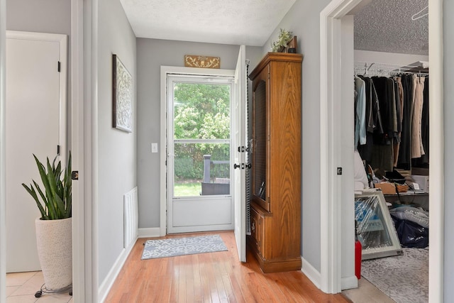 doorway with a textured ceiling, light wood-type flooring, and baseboards