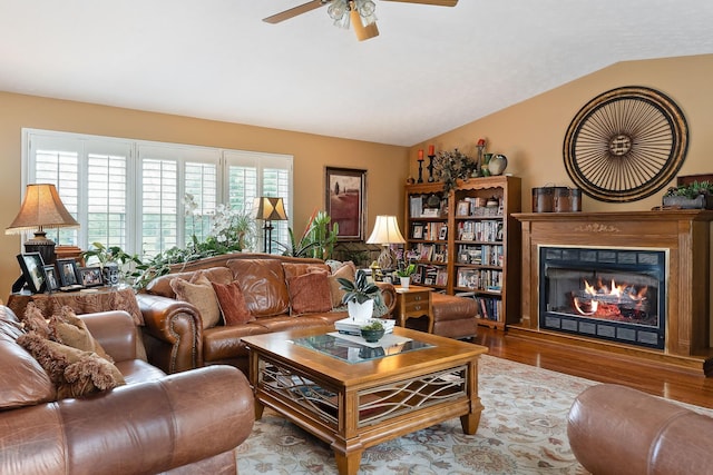 living room featuring wood finished floors, vaulted ceiling, a ceiling fan, and a glass covered fireplace