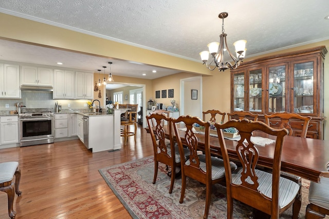 dining space with a chandelier, light wood-style floors, ornamental molding, recessed lighting, and a textured ceiling