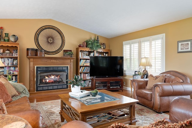 living room featuring vaulted ceiling, a warm lit fireplace, and wood finished floors