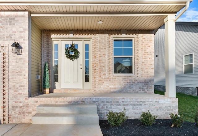 doorway to property featuring covered porch and brick siding