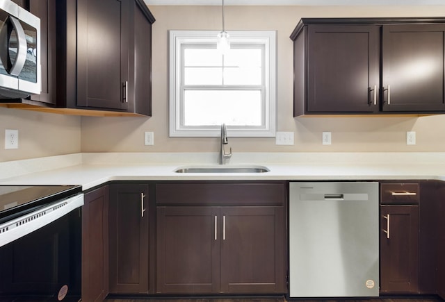 kitchen featuring appliances with stainless steel finishes, a sink, dark brown cabinets, light countertops, and hanging light fixtures