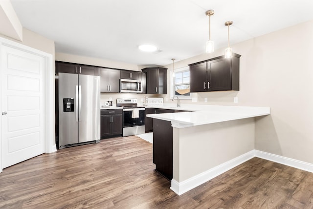 kitchen featuring appliances with stainless steel finishes, a peninsula, baseboards, a sink, and wood finished floors