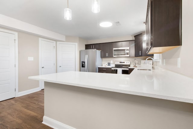 kitchen with stainless steel appliances, a sink, dark brown cabinetry, a peninsula, and dark wood-type flooring