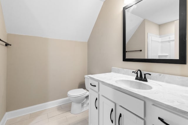 bathroom with vanity, toilet, lofted ceiling, and baseboards