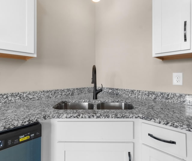 kitchen view of dishwasher, a sink, white cabinets, and light stone countertops