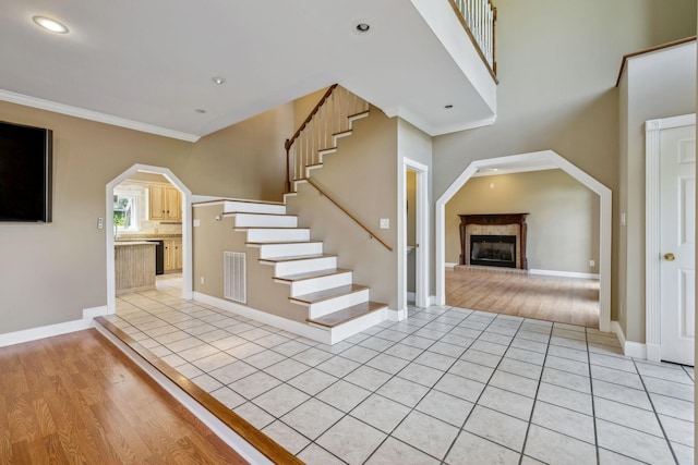 122 Windcrest Dr, Hohenwald, TN 38462 - unfurnished living room with a fireplace with raised hearth, arched walkways, light tile patterned floors, stairway, and crown molding
