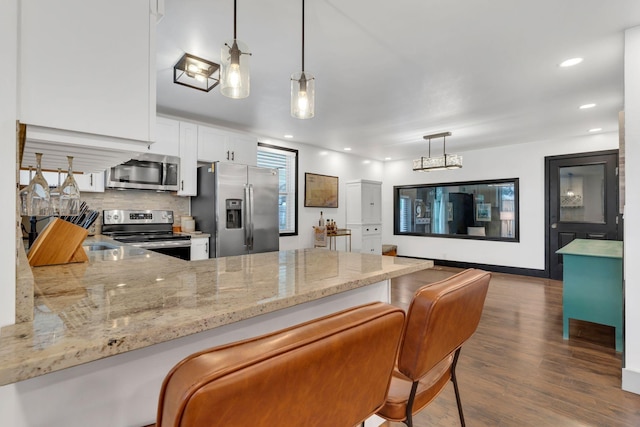 kitchen with appliances with stainless steel finishes, light stone counters, dark wood-type flooring, white cabinets, and a peninsula