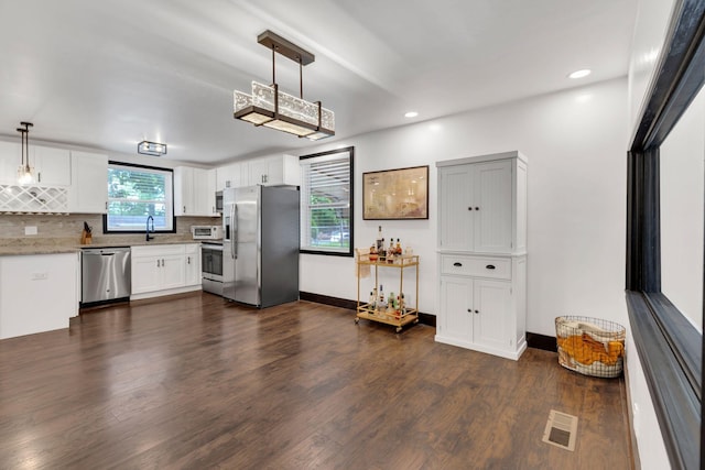 kitchen with appliances with stainless steel finishes, tasteful backsplash, dark wood finished floors, white cabinets, and a sink