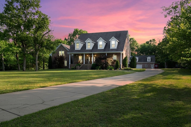 cape cod house featuring covered porch, a lawn, concrete driveway, and brick siding