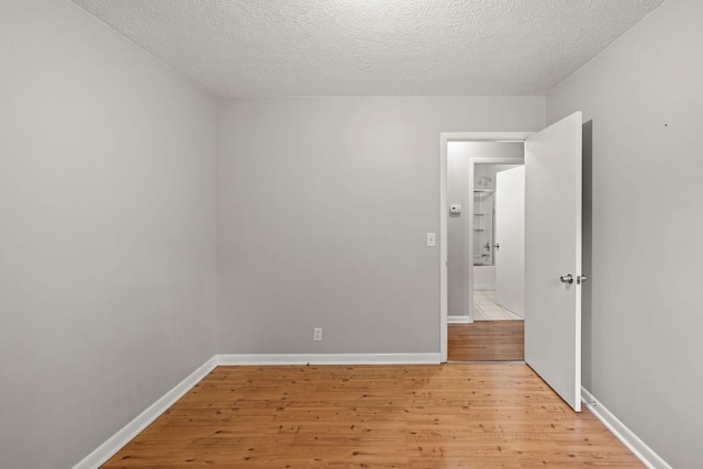 unfurnished bedroom with light wood finished floors, a textured ceiling, and baseboards
