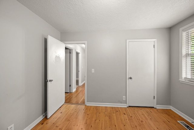 unfurnished bedroom with light wood-style flooring, baseboards, and a textured ceiling