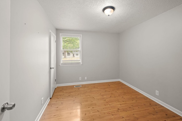 unfurnished room with a textured ceiling, light wood finished floors, and baseboards