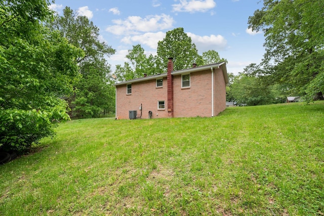 rear view of house featuring a chimney, brick siding, a yard, and central AC