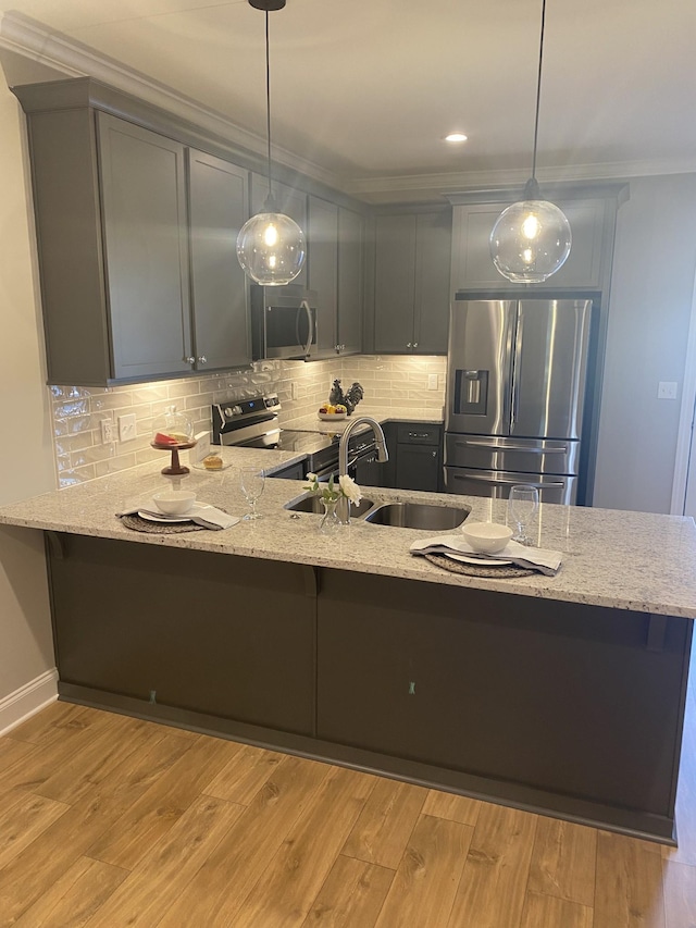 kitchen with stainless steel appliances, a sink, a peninsula, light stone countertops, and ornamental molding