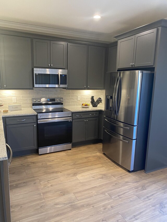 kitchen with stainless steel appliances, light stone countertops, decorative backsplash, ornamental molding, and light wood-style flooring