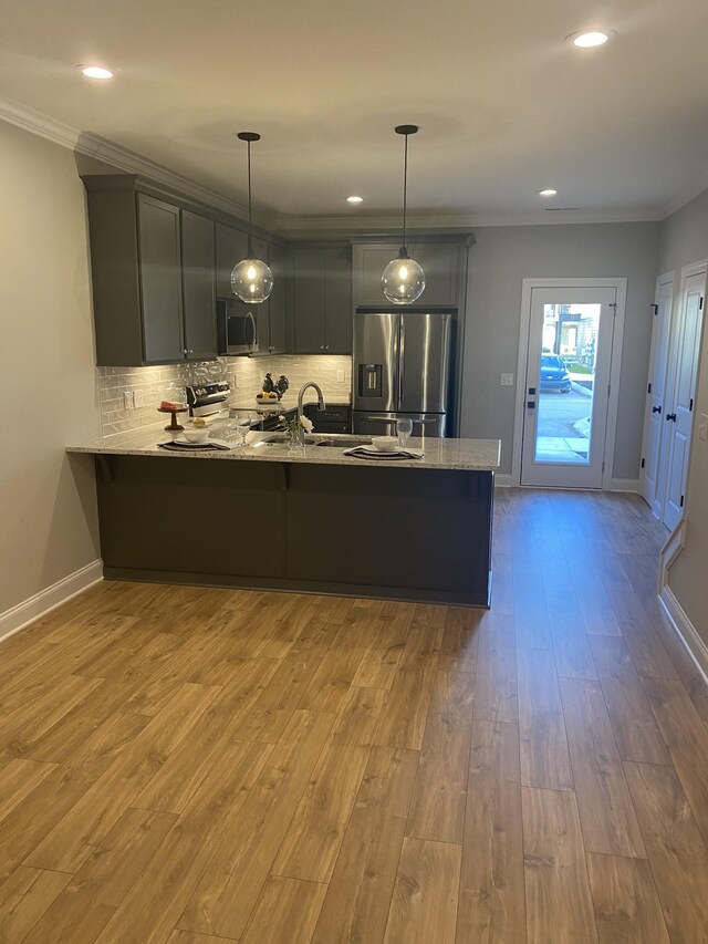 kitchen with stainless steel appliances, a peninsula, crown molding, wood finished floors, and decorative backsplash