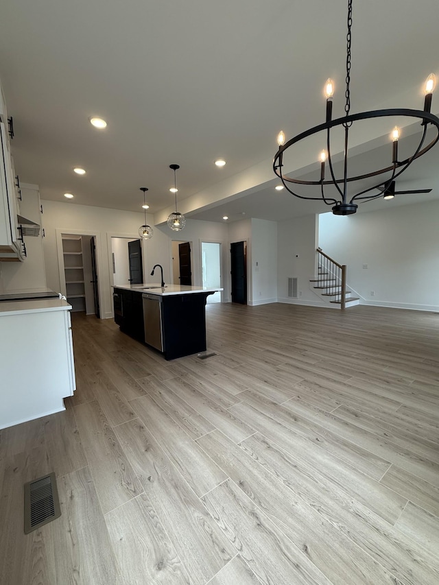 kitchen with open floor plan, a chandelier, a kitchen island with sink, light countertops, and light wood-type flooring