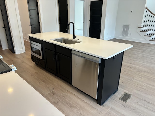 kitchen featuring appliances with stainless steel finishes, a sink, dark cabinetry, light wood-type flooring, and light countertops