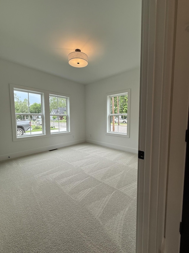 empty room featuring baseboards, healthy amount of natural light, and light carpet