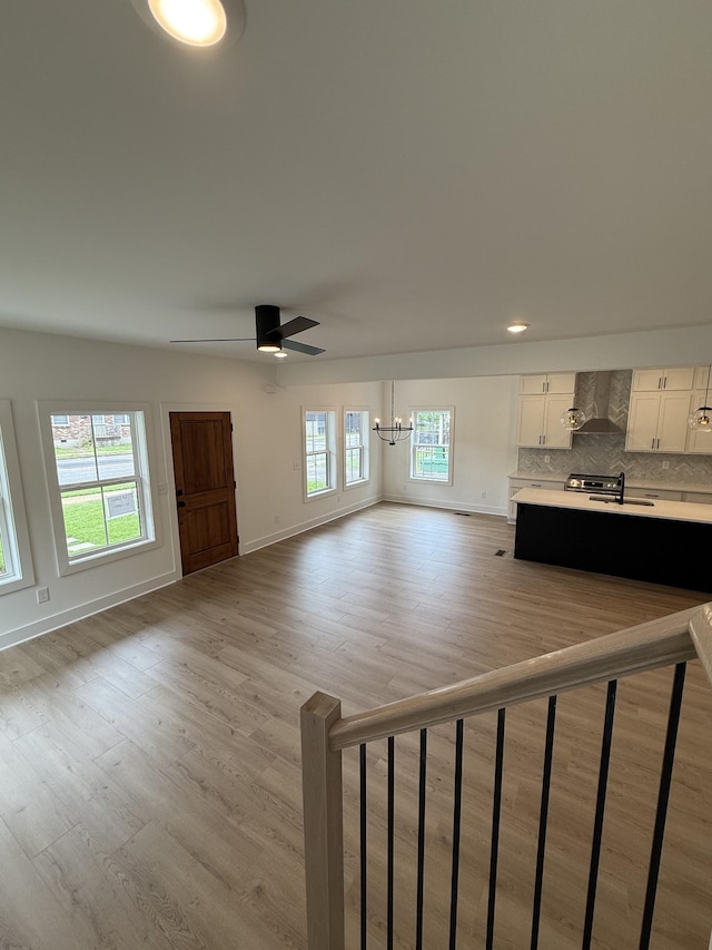 unfurnished living room with a chandelier, baseboards, light wood finished floors, and a sink