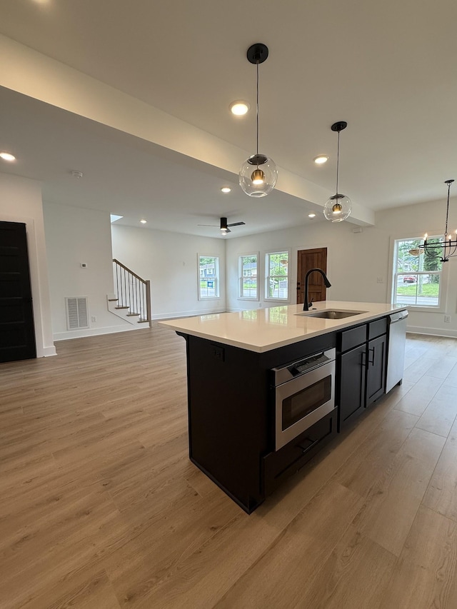kitchen with a sink, open floor plan, light wood-type flooring, stainless steel appliances, and dark cabinetry