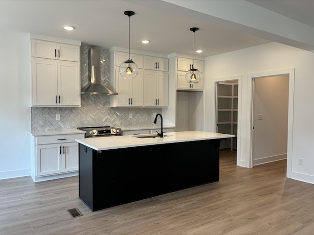 kitchen with a sink, wall chimney exhaust hood, light countertops, backsplash, and a kitchen island with sink