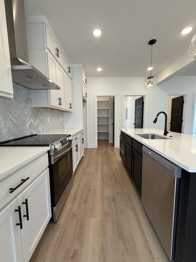 kitchen with wall chimney exhaust hood, stainless steel appliances, a sink, light countertops, and white cabinetry