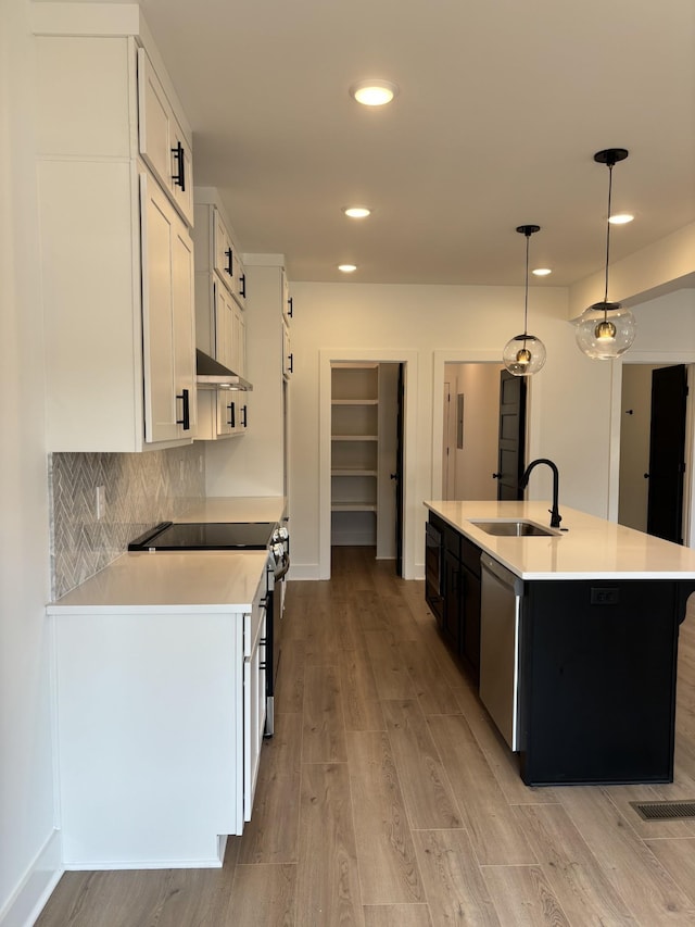 kitchen with a sink, appliances with stainless steel finishes, light wood finished floors, light countertops, and recessed lighting