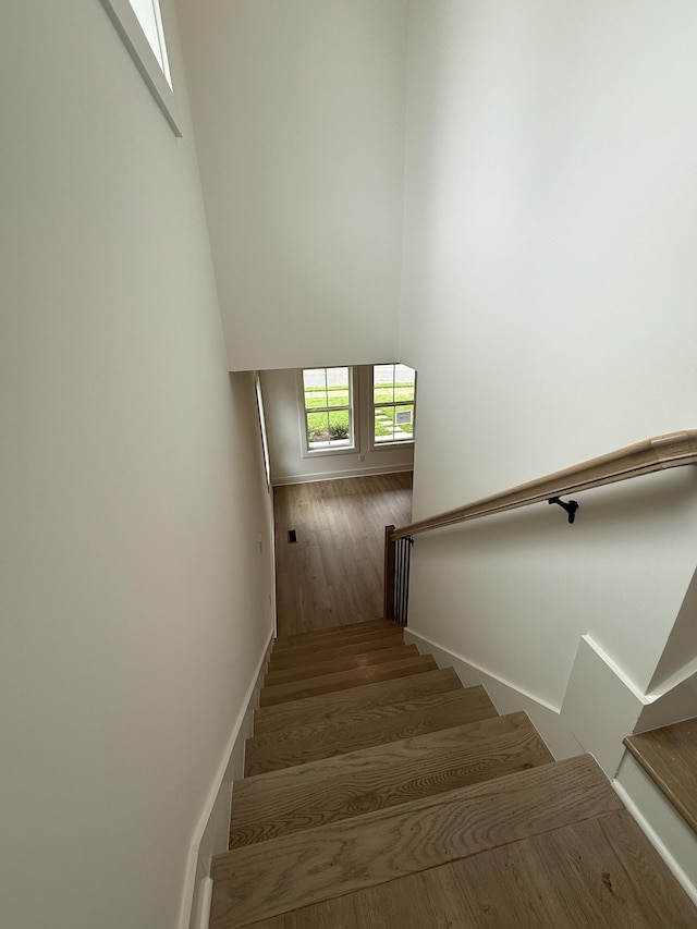 staircase with wood finished floors, baseboards, and a high ceiling