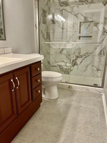 full bath with vanity, a marble finish shower, and toilet