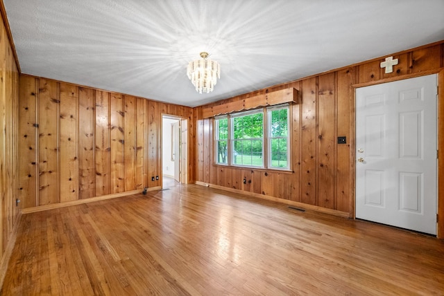 empty room featuring a chandelier, baseboards, light wood-style floors, and wooden walls