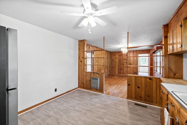 kitchen with freestanding refrigerator, heating unit, wooden walls, brown cabinets, and a ceiling fan