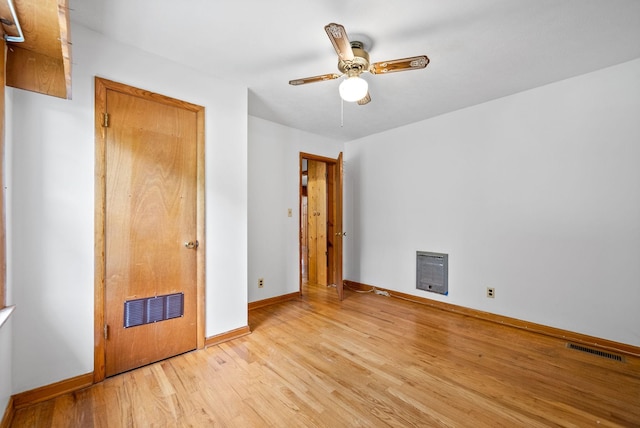 unfurnished bedroom with heating unit, light wood-type flooring, baseboards, and a ceiling fan