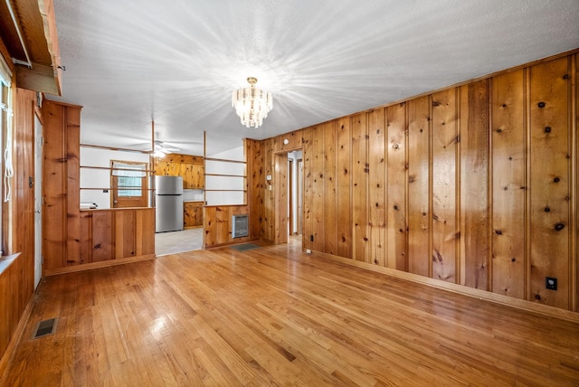 unfurnished living room with light wood-style flooring, a chandelier, and wood walls