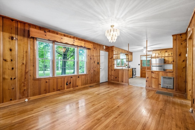 unfurnished living room with light wood-style floors, wood walls, a chandelier, baseboards, and heating unit