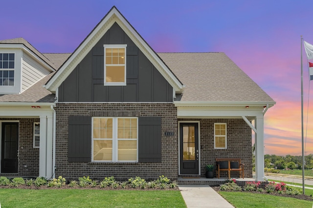 view of front of house with brick siding, board and batten siding, a porch, a shingled roof, and a front lawn