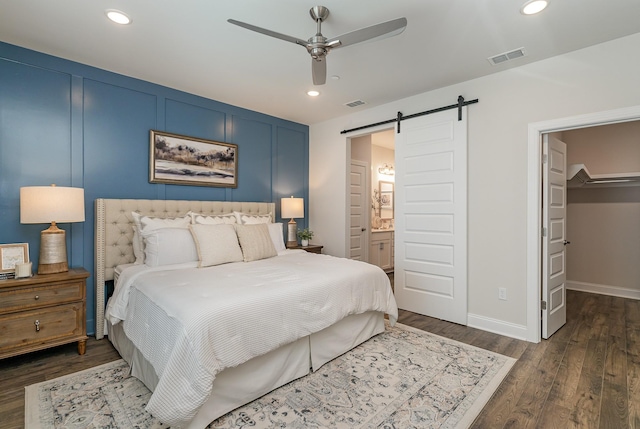 bedroom with a barn door, dark wood-style floors, recessed lighting, a spacious closet, and connected bathroom