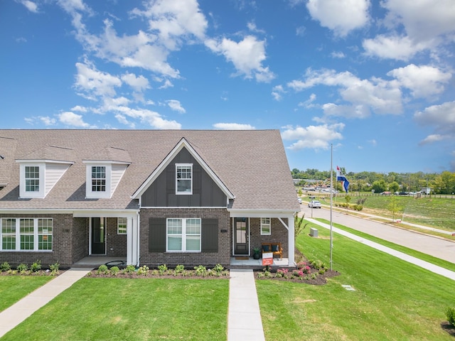 view of front of property featuring brick siding, covered porch, a front lawn, and board and batten siding