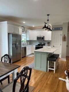 kitchen with appliances with stainless steel finishes, light countertops, light wood-style flooring, white cabinets, and a kitchen island