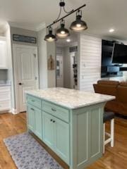 kitchen featuring green cabinetry, light countertops, a kitchen island, light wood-type flooring, and hanging light fixtures