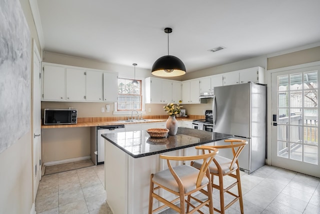 kitchen with appliances with stainless steel finishes, a sink, a center island, white cabinetry, and pendant lighting
