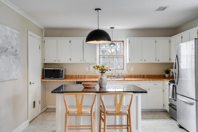 kitchen featuring freestanding refrigerator, a sink, light tile patterned flooring, a kitchen island, and white cabinetry